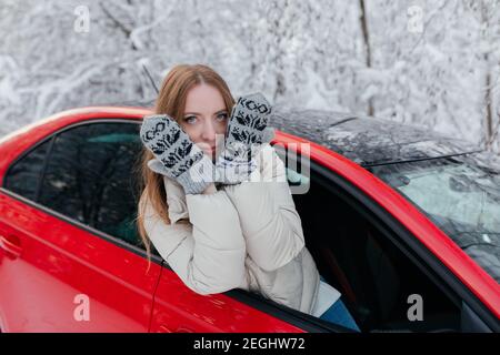 Glückliche Frau schaut aus dem Autofenster und bedeckt ihr Gesicht mit ihren Händen. Winterwald. Stockfoto