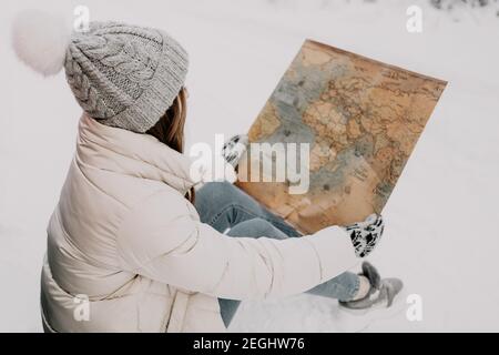 Eine junge Frau sitzt im Schnee und hält eine Karte in den Händen. Reisekonzept. Stockfoto