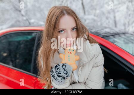 Glückliche Frau schaut aus dem Autofenster, hält ein Cookie in Form eines Mannes in den Händen. Winterwald. Stockfoto