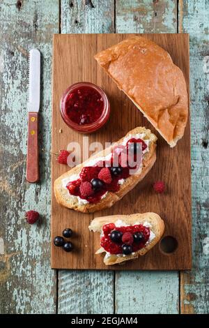 Hausgemachte Beerenmarmelade mit frischen Himbeeren und Johannisbeeren auf Ciabatta Toasts auf hölzernen Schneidbrettern Draufsicht Stockfoto