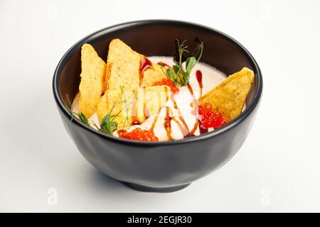 Cremige Lachssuppe in einer schwarzen Kutsche. Zutaten Sahne, Lachs, Pflanzenöl, Lachskaviar, Teriyaki-Sauce, Nachos Chips, Salz. Für die Speisekarte des Restaurants. Stockfoto