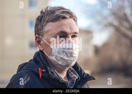 Porträt eines Mannes mittleren Alters in einer Schutzmaske, der vor dem Hintergrund eines Stadtbildes steht. Konzept der neuen Realität, Virenschutz. Stockfoto