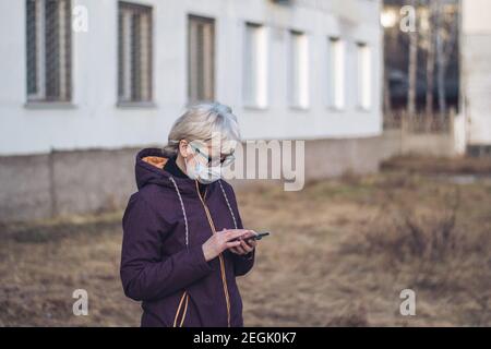 Eine Frau mittleren Alters in einer Schutzmaske steht in einer fremden Stadt, sucht einen Weg, Blick auf ein Smartphone, mit einer Anwendung, GPS. Stockfoto