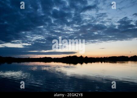 Lebendige Farben bei Sonnenuntergang, Blick über einen ruhigen See. Blauer, gestromter Makrelenhimmel, sanftes orangefarbenes Licht, ruhiges, windloses Wasser. Norfolk Bro Stockfoto