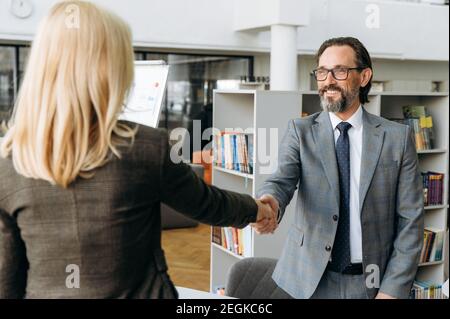 Intelligente männliche Leiter des Unternehmens schüttelt die Hände mit blonden Haaren Frau im Interview, er genehmigte Frau für einen Job, kommen zu einer Einigung über Verhandlungen, gutes Geschäft Stockfoto