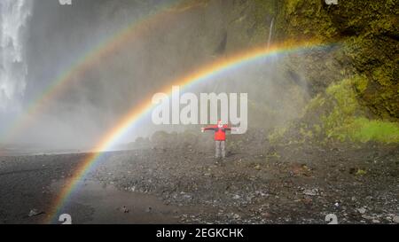 Skogar, Island - Mai 2019: Mann steht unter dem Regenbogen im Skogafoss Wasserfallgebiet Stockfoto