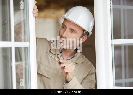 Glasurstecker, der den Schraubendreher an einem offenen pvc-Fenster hält Stockfoto