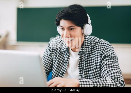 Junge fröhlich asiatische Student mit Video-Anruf auf Laptop in Schulungsraum Stockfoto