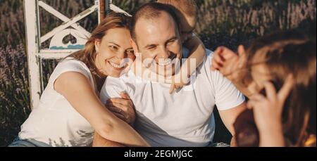 Kaukasische Familie sitzt in einem Lavendelfeld lächelnd und umarmt An einem sonnigen Tag Stockfoto