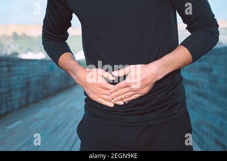 Mann in schwarzen Sportkleidung leiden unter Magen Seitenstich oder Krämpfe während des Laufens. Seitenschmerzen nach dem Joggen. Stockfoto