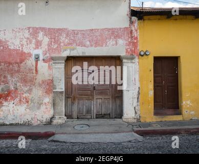 Verwitterte Wand mit gelb-rot und weiß Farbe, Holztüren und Kopfsteinpflaster Steinstraße Stockfoto
