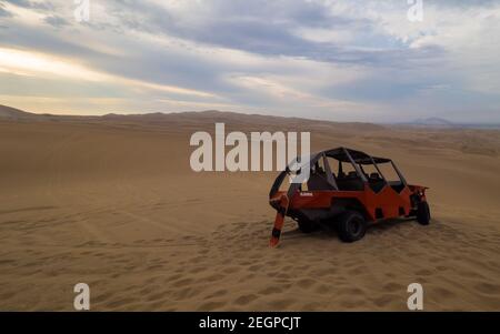 Peru, Ica - 21. September 2019 - Buggy und Sandbrett bei Sonnenuntergang in der Wüste, Sanddünen im Hintergrund Stockfoto