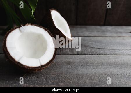 Gebrochene Kokosnüsse auf grauem Holzhintergrund mit Palmblatt. Weißes Kokosnusspulpe Stockfoto