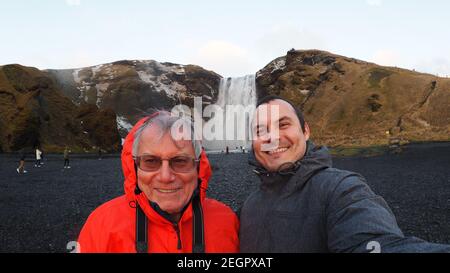 Vater und Sohn lachen mit Skogafoss Wasserfall dahinter Stockfoto
