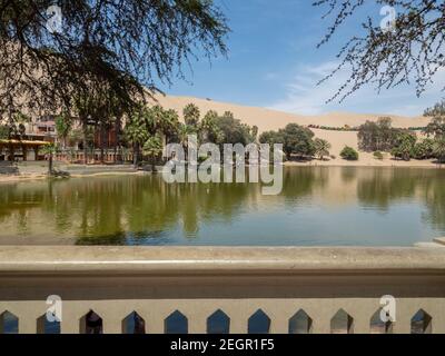 Blick auf den See in der Oase huacachina Palmen rund um das Wasser, im Hintergrund Sanddünen und Buggys Stockfoto