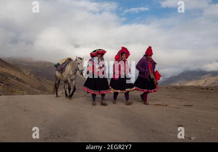 Peru, Vinicunca - 1. Oktober 2019 - drei gebürtige Frauen gehen und reden ein Pferd zu führen, während sie auf einer unbefestigten Straße in traditioneller Kleidung gehen Stockfoto