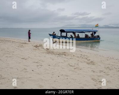 Panama, San Blas - 18. Mai 2019 Touristen steigen an Bord eines kleinen Bootes auf den Sanblas Inseln, guna yala Flagge Wellen an den windbewölkten Tag, Sand im Vordergrund Stockfoto