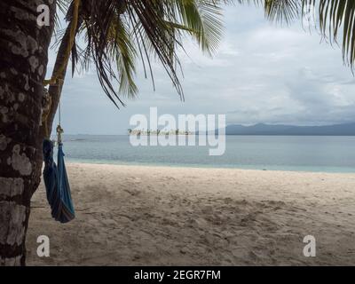 Blick auf die Insel von einer anderen Insel, mit einer Hängematte und Palmen in san blas panama, Guna yala, Bergkette und Insel im Hintergrund Stockfoto