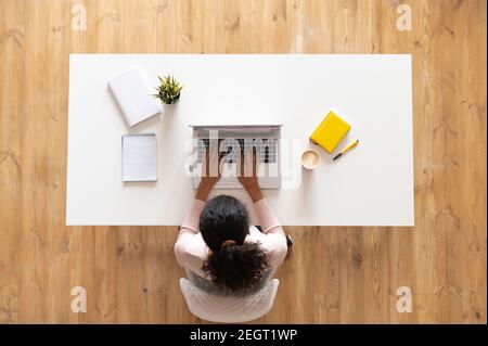 Ansicht von oben auf gemischte ethnische Frauen oder freiberufliche Frauen mit lockigen Haaren sitzen am weißen Tisch Schreibtisch mit gut organisierten Raum, tippen auf der Stockfoto