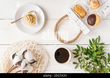 Draufsicht der Anordnung von verschiedenen Mini-Kuchen auf Teller und Tablett, Tasse Kaffee und grüne Blätter auf weißem Hintergrund. Stockfoto