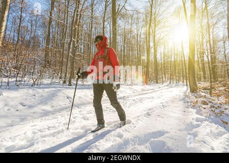 Mann in Outdoor-Ausrüstung Wandern durch verschneiten Wald in der Winter mit schönem Sonnenlicht Stockfoto