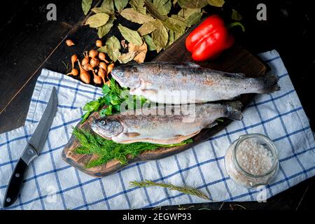 Zwei rohe Regenbogenforellen mit Garnierung auf einem Holzbrett. Stockfoto