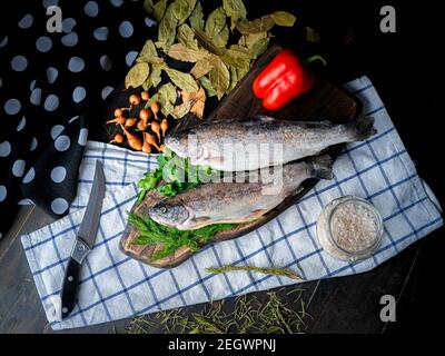 Zwei rohe Regenbogenforellen mit Garnierung auf einem Holzbrett. Stockfoto