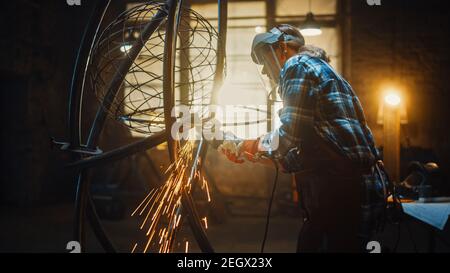 Talentierte innovative Tomboy Female Artist verwendet einen Angle Grinder, um eine abstrakte, brutale und ausdrucksstarke Metallskulptur in einem Workshop zu machen. Modern Stockfoto