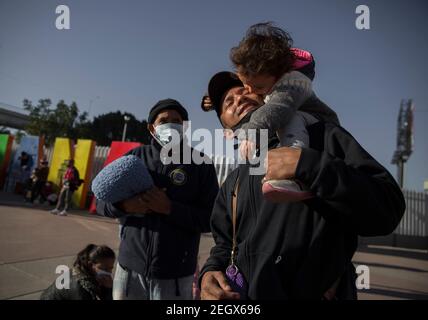 18. Februar 2021, Mexiko, Tijuana: Ein Mann zentralamerikanischer Herkunft hält seinen Sohn, nachdem er am Grenzübergang protestiert hat. Zentralamerikanische und mexikanische Migranten, die Flüchtlinge im Flüchtlingsheim Agape sind, demonstrierten vor dem Haupteingang des Grenzübergangs El Chaparral an der Grenze zwischen Tijuana, Mexiko, Und San Diego, Kalifornien, mit dem Ziel, die US-Behörden zu bitten, die Grenze zu öffnen und den Prozess der Gewährung von politischem Asyl für Flüchtlinge neu zu starten. Nach dem Richtungswechsel in der Migrationspolitik erlaubt die US-Regierung erneut Asylsuchende über die Grenze. So Stockfoto