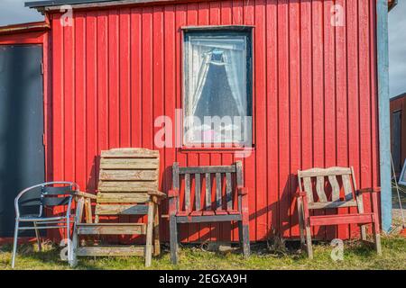 Traditionelle skandinavische Sommerhausfassade mit rechteckigem Fenster und alten Stühlen Gegen die rote Holzfassade aus Planken und Fischen Dekoration Stockfoto