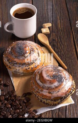 Zwei süße Brötchen mit Mohn und einer Tasse Kaffee Auf dunklem Holztisch Stockfoto