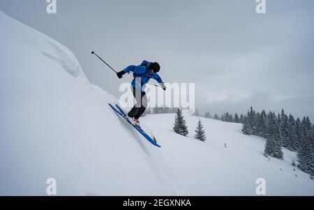 Skifahrer Skifahren in hohen Bergen bei windigem, kaltem Wetter. Schnee fällt von schweren grauen Wolken. Winter Web Banner Design. Stockfoto