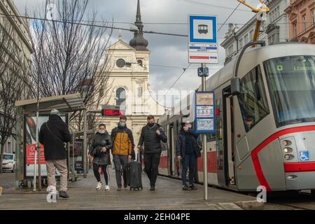 Brünn, Tschechische Republik. 02-17-2021. Menschen mit Gesichtsmaske, um Corona-Virus auf Cheska Straßenbahnhaltestelle mit Kirche St. Thomas auf dem Hintergrund in der Stadt zu schützen Stockfoto