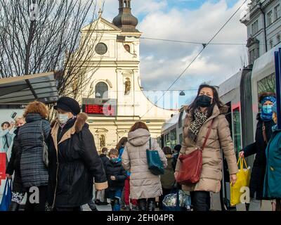 Brünn, Tschechische Republik. 02-17-2021. Menschen mit Gesichtsmaske, um Corona-Virus auf Cheska Straßenbahnhaltestelle mit Kirche St. Thomas auf dem Hintergrund in der Stadt zu schützen Stockfoto