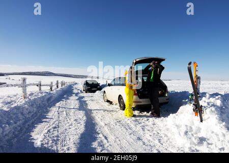 Schneeszene mit Wintersportlern, ein Auto parkt an einer verschneiten Straße, Tschechische Republik Skifahren in den tschechischen Bergen Winterszene Krusne Hory Erzgebirge Stockfoto