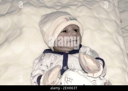 Nahaufnahme Portrait Bild von niedlichen schönen liebenswert Baby junge asiatische und indische Ethnizität in Winterkleidung liegen des Bettes auf weißer Decke. Einen Monat alt Stockfoto