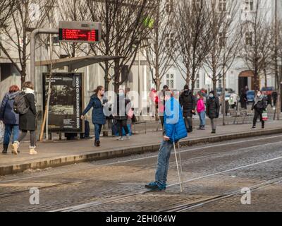 Brünn, Tschechische Republik. 02-17-2021. Handicap Mann überquert Tramschienen mit Gehstöcken mit Gesichtsmaske vor Corona Virus zu schützen Spaziergang auf Cheska Straßenbahn Stockfoto