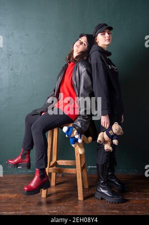 Zwei Teenager-Mädchen im Grunge-Stil gekleidet, gegen eine dunkelgrüne Wand.Weiche Spielzeuge in den Händen der Mädchen. Stockfoto