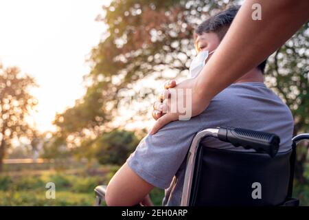 Nahaufnahme Patient oder behinderter Mann sitzt im Rollstuhl und junge Sohn auf einem Spaziergang in der Natur Frühling. Stockfoto