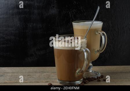 Zwei Glasplatten mit Cappuccino und Eisschokolade auf einem Holztisch mit schwarzem Strukturhintergrund. Selektiver Fokus. Stockfoto