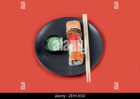 Sushi-Mix rollt auf einem schwarzen Teller auf rotem Hintergrund Stockfoto