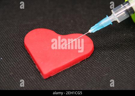 Medizinische Spritze und ein Herz. Herzförmiges Objekt und eine Heilung. Stockfoto