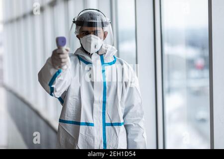 Medizinische Mitarbeiter Scannen mit Infrarot-Thermometer, IR-Thermoscan. Zuversichtlich asiatische Arzt in schützenden PSA Anzug trägt Gesichtsmaske und Brillen in ho Stockfoto