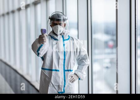 Medizinische Mitarbeiter Scannen mit Infrarot-Thermometer, IR-Thermoscan. Zuversichtlich asiatische Arzt in schützenden PSA Anzug trägt Gesichtsmaske und Brillen in ho Stockfoto