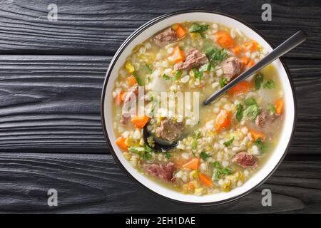 Hausgemachte Lammbrühe mit Wurzelgemüse, Gerste und Erbsen aus der Nähe in einer Schüssel auf dem Tisch. Horizontale Ansicht von oben Stockfoto