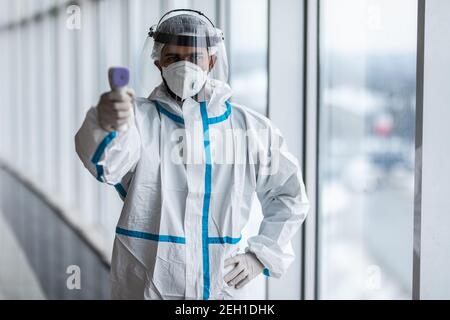 Medizinische Mitarbeiter Scannen mit Infrarot-Thermometer, IR-Thermoscan. Zuversichtlich asiatische Arzt in schützenden PSA Anzug trägt Gesichtsmaske und Brillen in ho Stockfoto