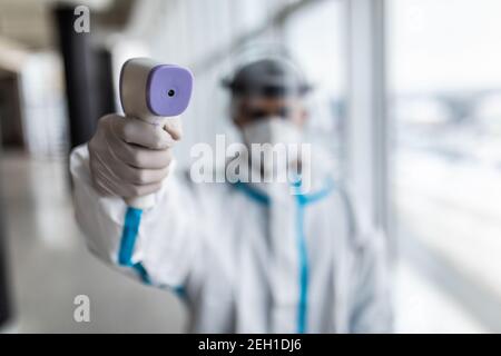 Medizinische Mitarbeiter Scannen mit Infrarot-Thermometer, IR-Thermoscan. Zuversichtlich asiatische Arzt in schützenden PSA Anzug trägt Gesichtsmaske und Brillen in ho Stockfoto