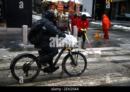 New York, Usa. Februar 2021, 18th. Ein Fahrrad-Lieferer fährt an Arbeitern vorbei, die während eines Schneesturms am Times Square den Schnee räumen.der US-Wetterdienst gab eine Winterwetterempfehlung für den zweiten Schneesturm der Woche heraus. Bis zu 8 Zoll Schnee sollen sich im Laufe von zwei Tagen ansammeln. Kredit: SOPA Images Limited/Alamy Live Nachrichten Stockfoto