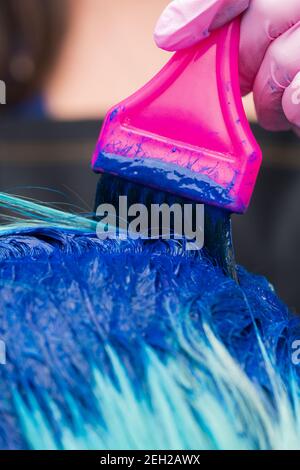Friseur in Schutzhandschuh mit magentafarbenen Pinsel beim Auftragen von blauer Farbe auf smaragdgrüne Haarfarbe, während des Färbeprozesses Haar in stilvoller Farbe Stockfoto