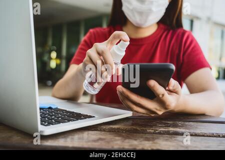 Nahaufnahme Asiatische Frau mit Desinfektionsmittel Alkohol für die Reinigung von Mobiltelefonen vor der Arbeit mit Technologie Laptop, von zu Hause aus in Covid-19 Pandemie, s Stockfoto